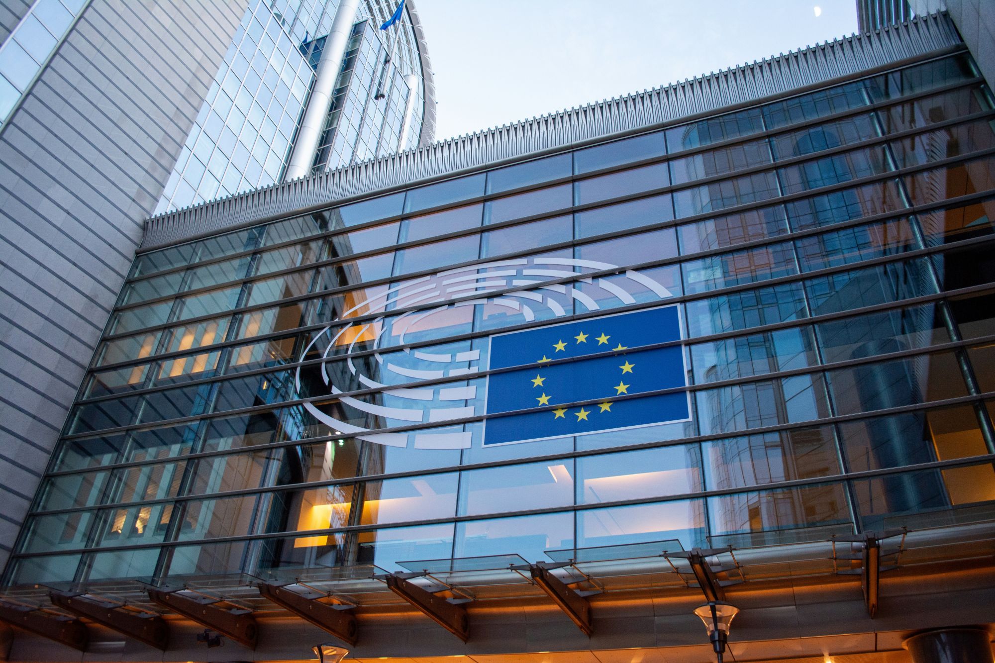 European Parliament building in Brussels with the EU flag and the Parliament logo on its glass façade