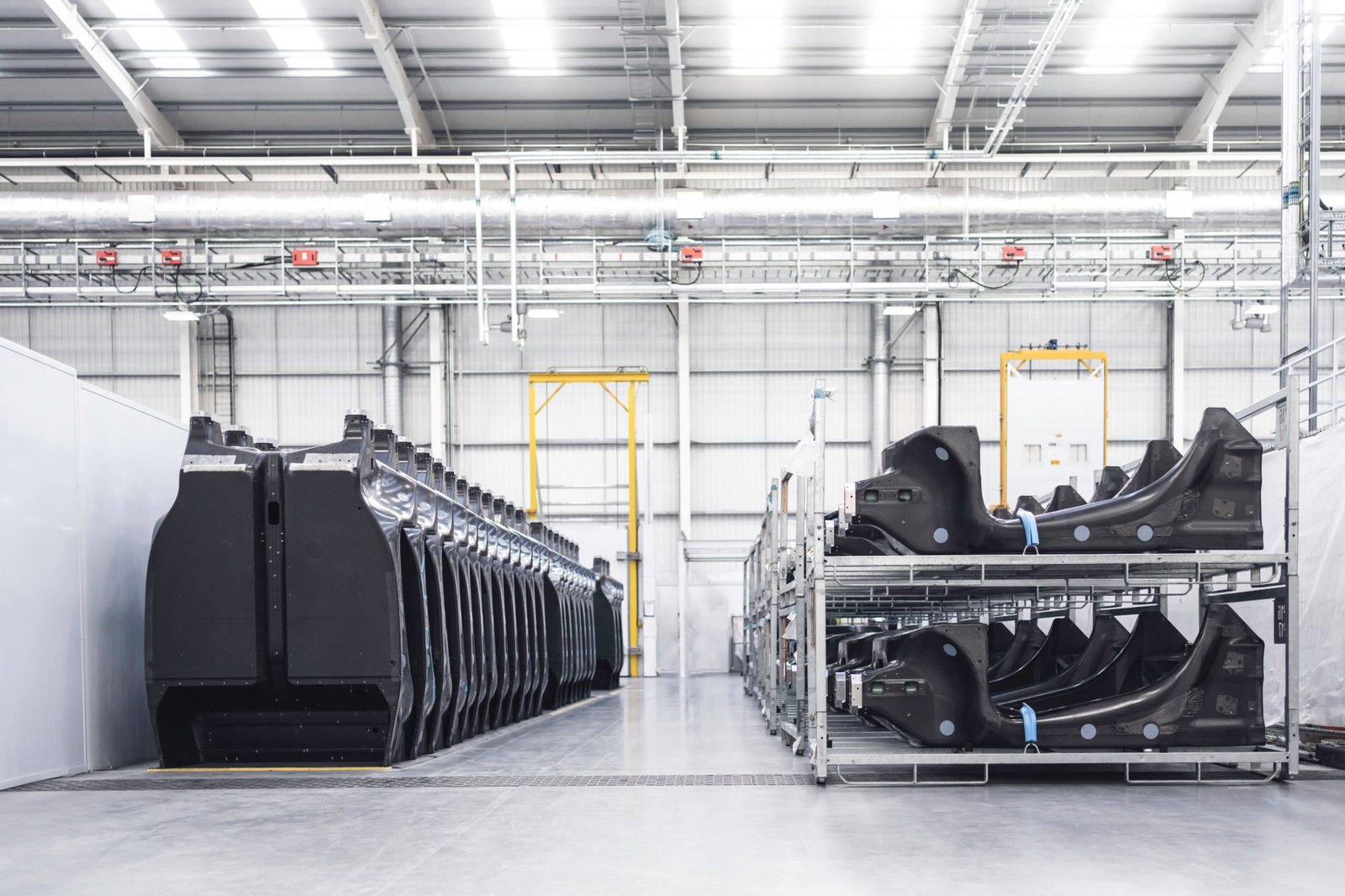 Rows of black carbon-fibre chassis structures lined up and stacked on racks in a bright production hall