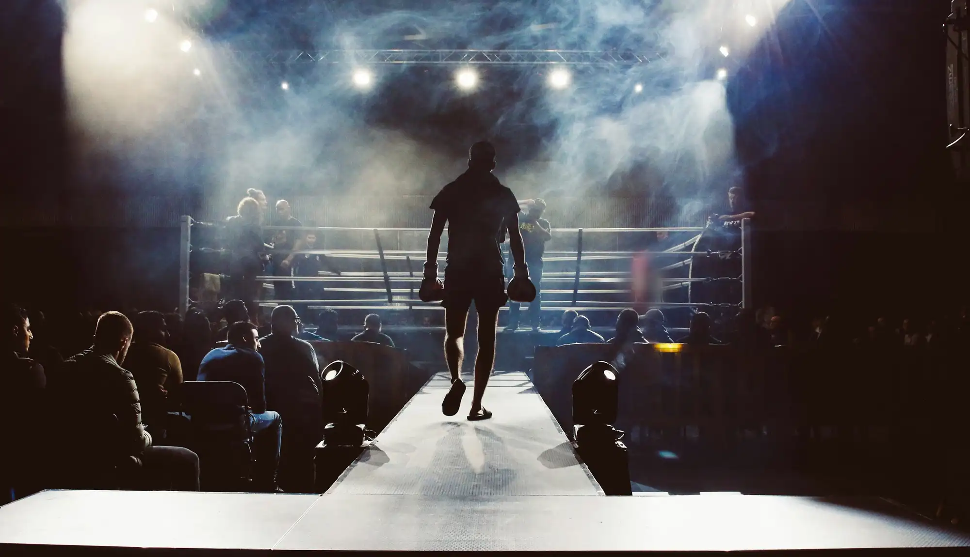 A fighter walks out through the crowd towards a lit ring