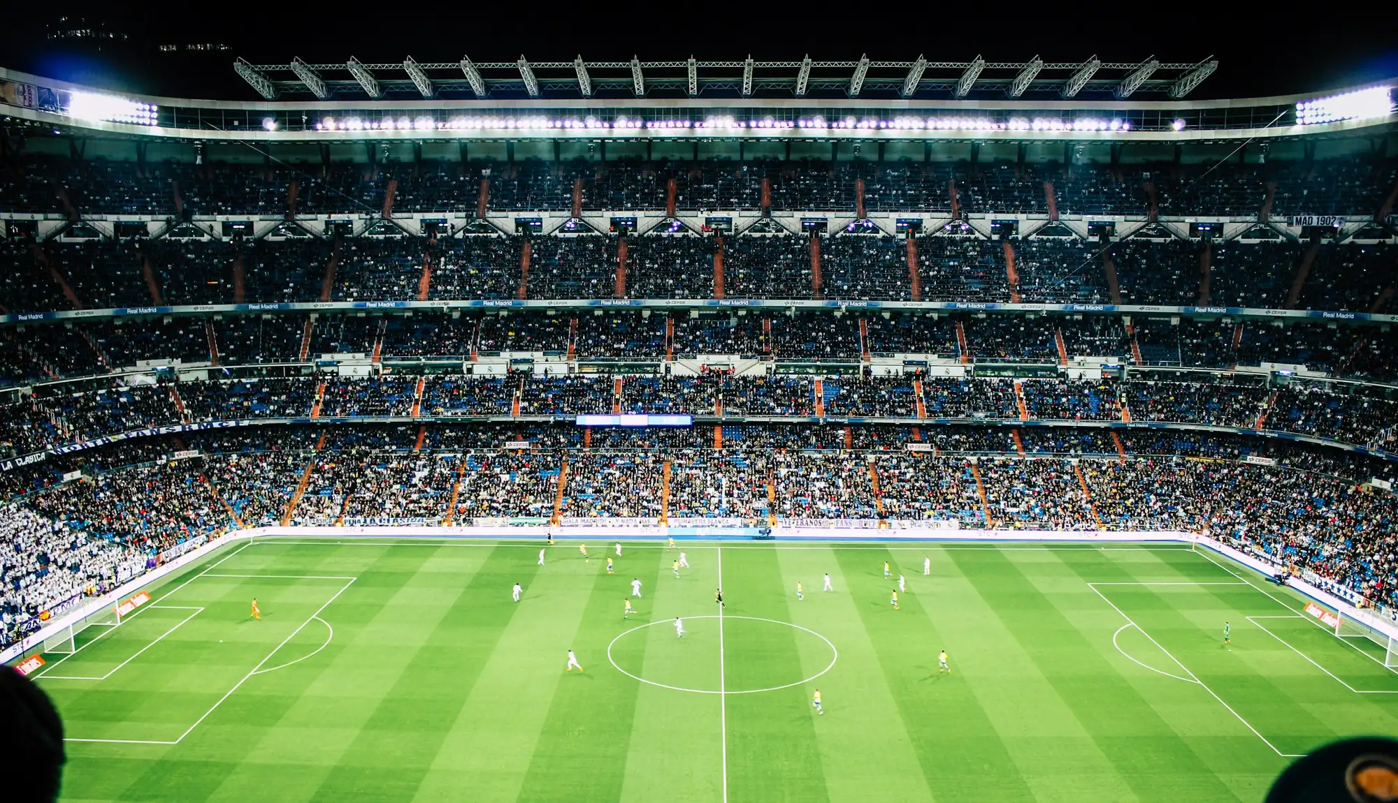 Floodlit football stadium at night, seen from the upper stands