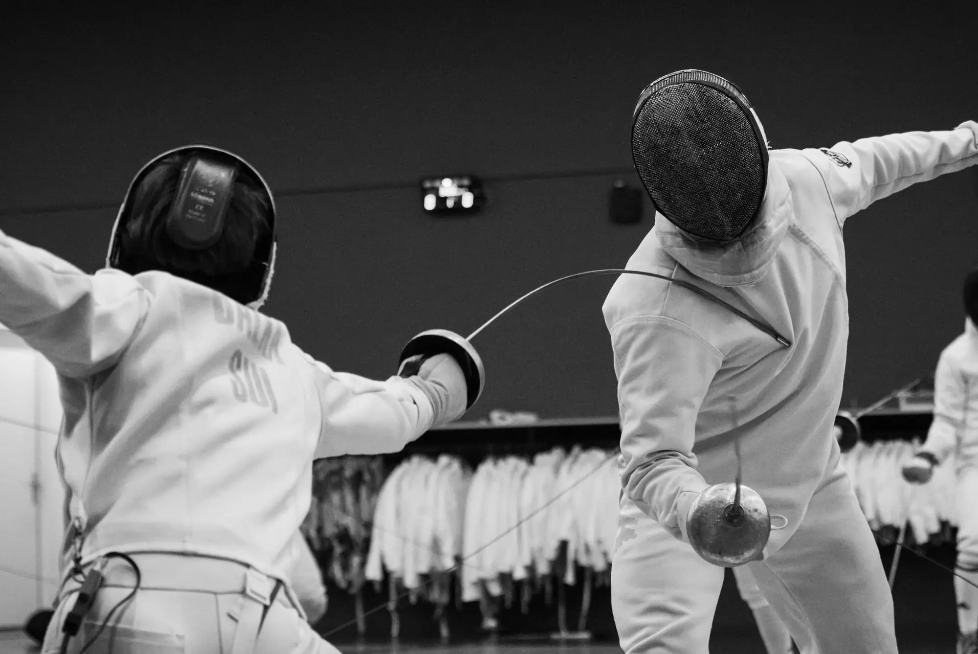 Two fencers mid-bout, one lunging with the blade bent against the other